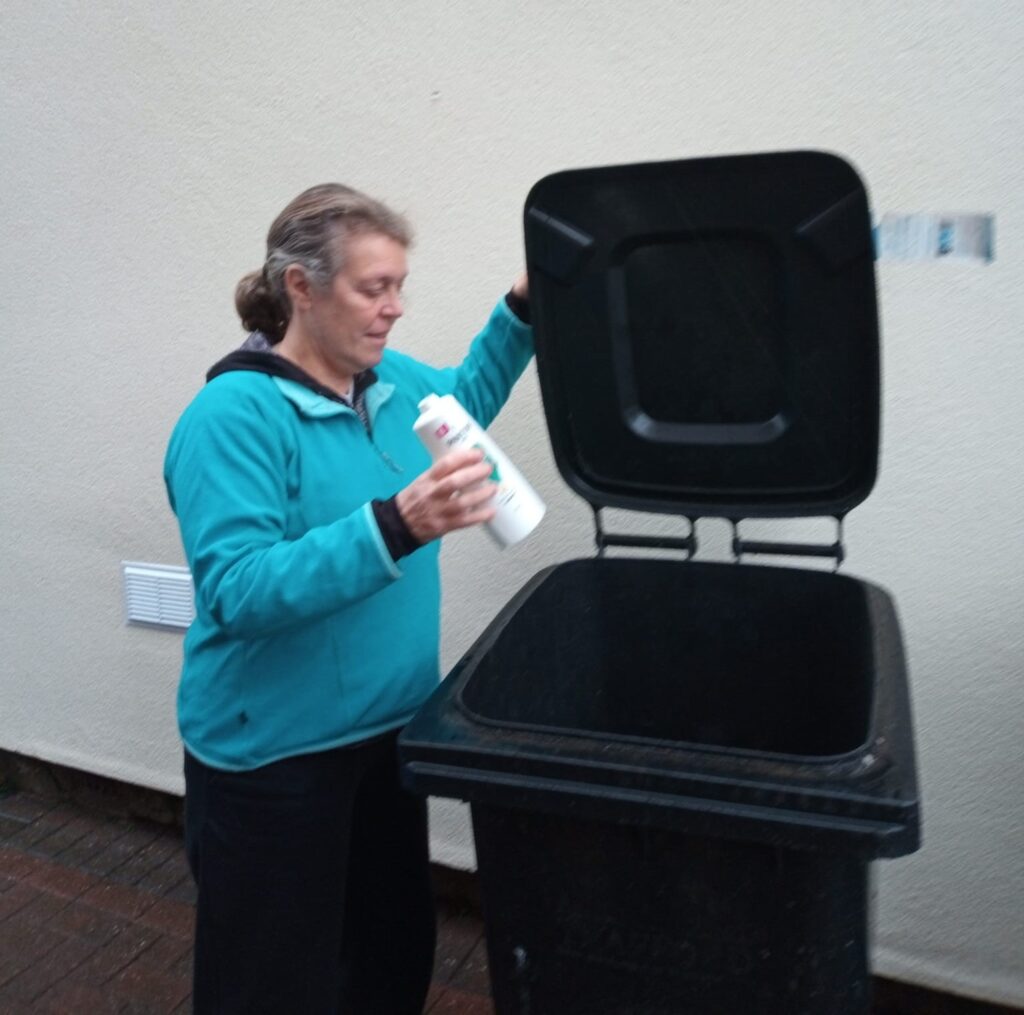 Image of Trafford Green Party Councillor Jane Leicester using a black plastic recycling bin